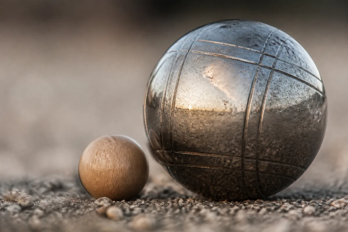 Boule de pétanque et but en bois posés sur un terrain de gravier fin