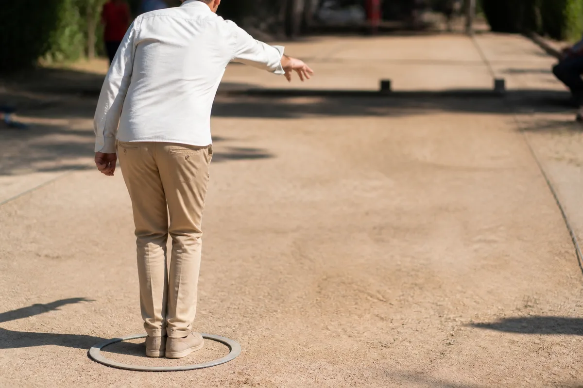 Joueur de pétanque de dos, pieds joints dans un cercle tracé au sol, bras en fin de lancer