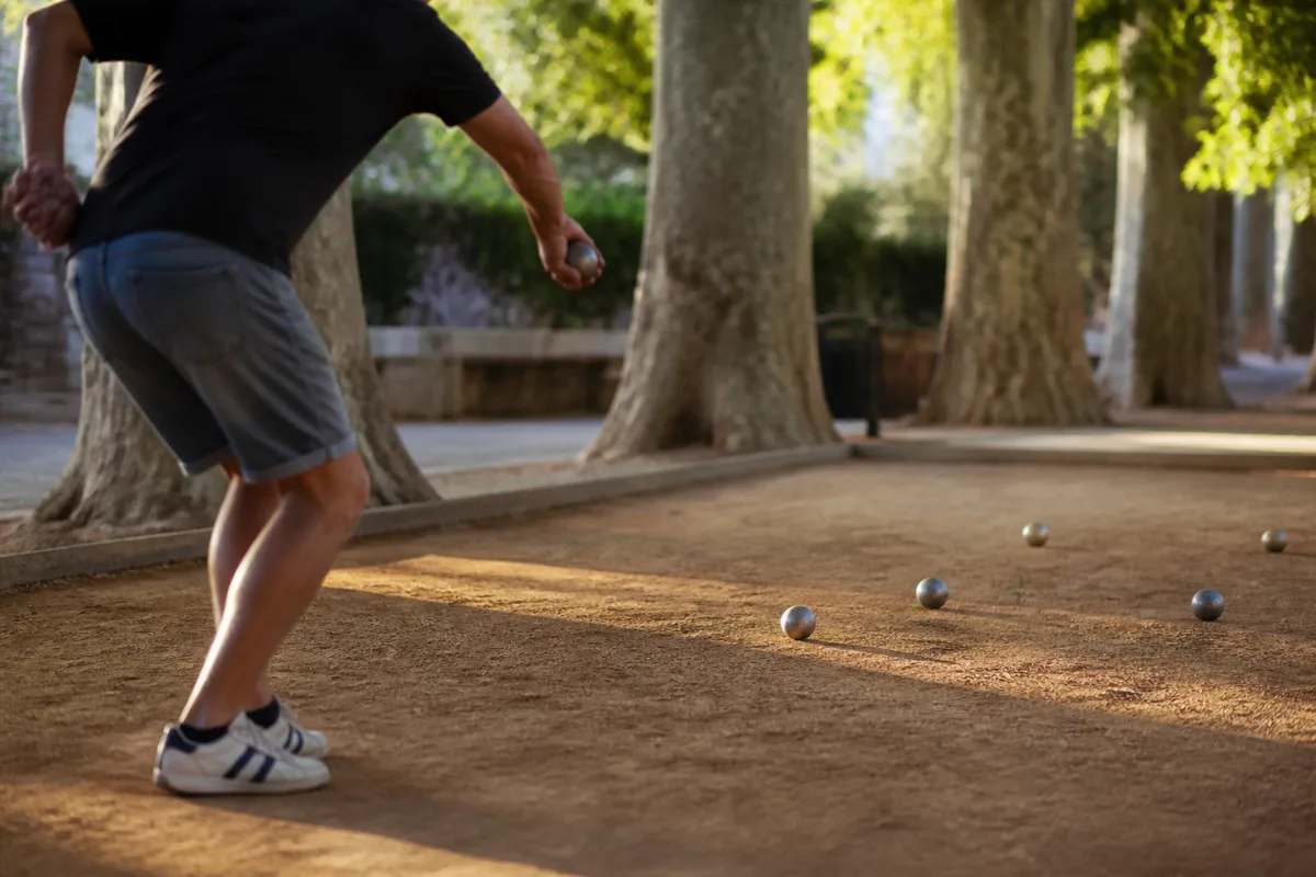 Joueur en pleine action de tir sur un terrain de boules, bras armé
